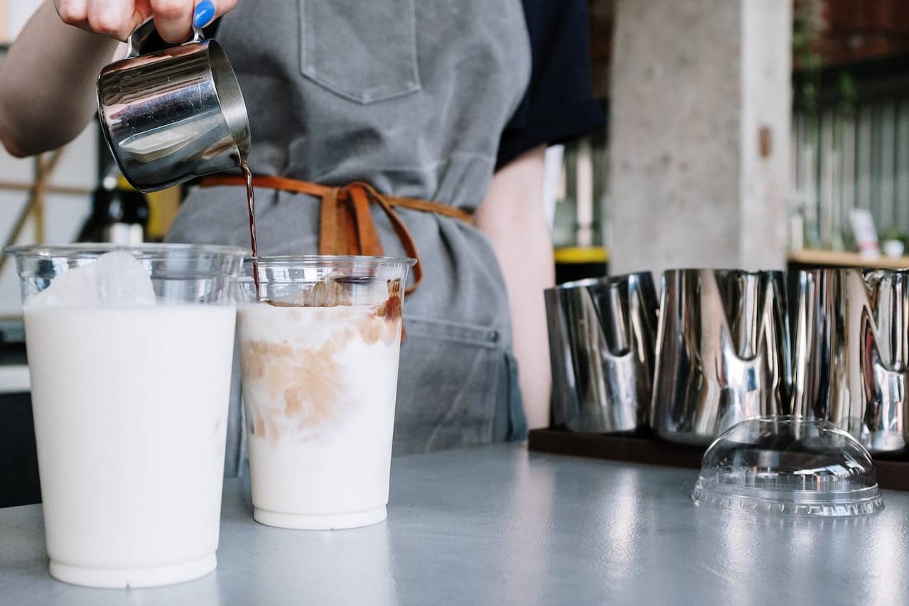 barista pouring espresso into cold milk filled cups