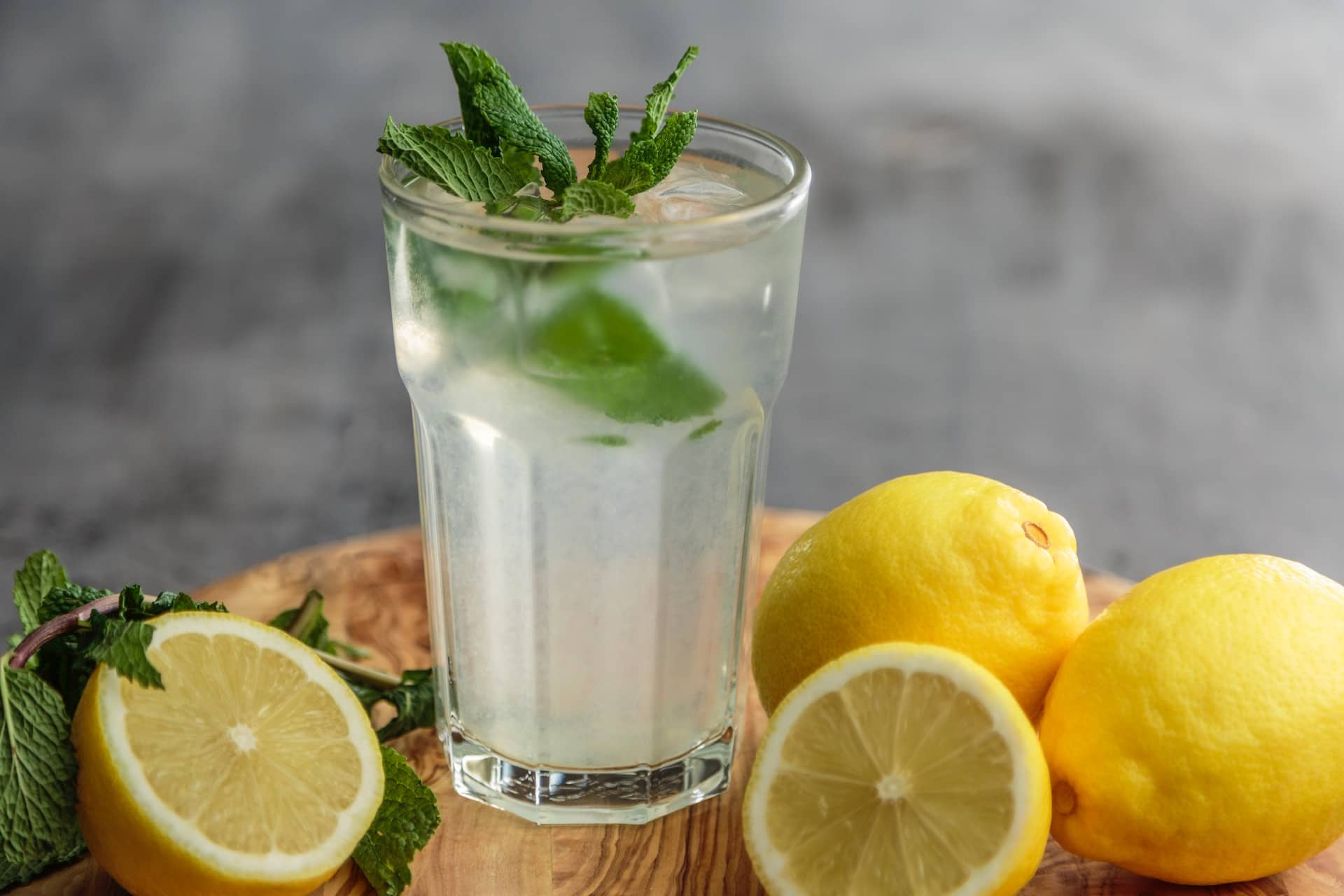 drink in glass with mint leaves on top lemons on wooden table surrounding
