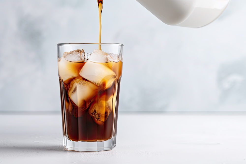 Someone pouring coffee over ice in a glass