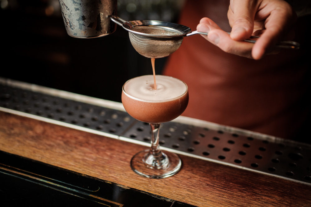 A barista pouring espresso martini on a cocktail glass